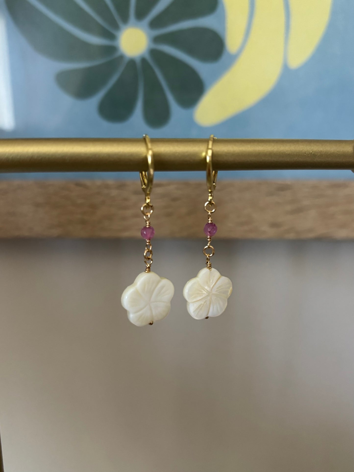 Close-up of Hibiscus Dangle Earrings featuring white carved shell flowers, black shark teeth, and pink gemstones. Suspended on 18k gold-plated hooks with 14k gold-filled wire. Ocean and flower-inspired earrings perfect for summer looks, beach brides, or tropical escapes. Part of Soul Wave Beach Co.’s handcrafted coastal jewelry collection.