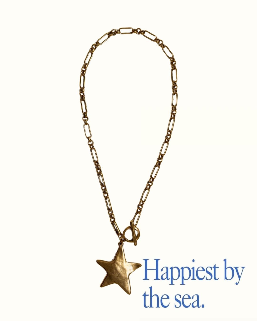 A bold gold chain necklace with a toggle clasp and chunky starfish pendant is styled on a cream background with the phrase “Happiest by the sea” in soft blue serif font. The necklace from Soul Wave Beach Co’s Ocean Heritage collection blends coastal charm with statement-making design, inspired by the texture and shimmer of ocean treasures. This beach-inspired accessory radiates sunshine and salty air, perfect for layering with other gold pieces or standing out solo.