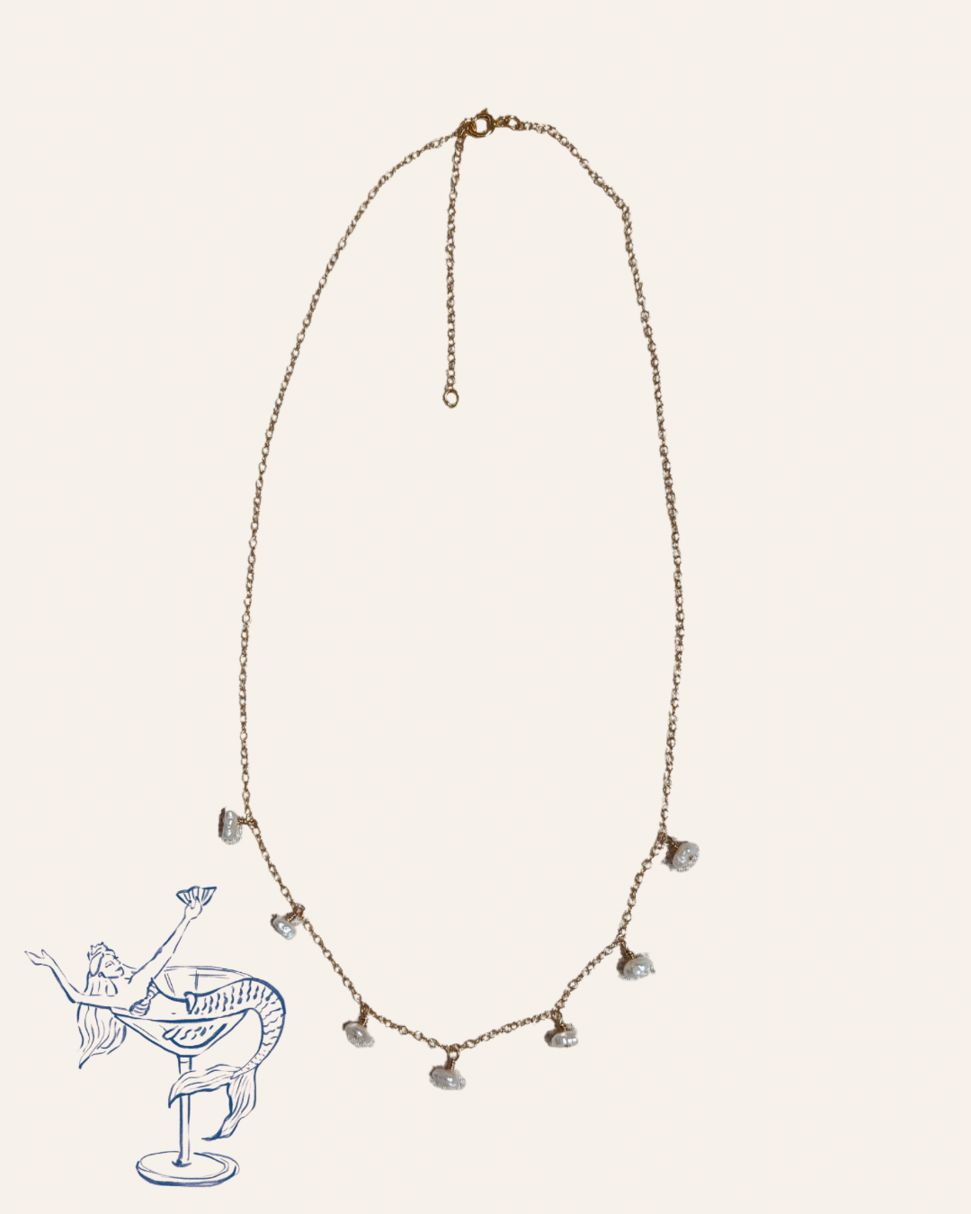 Gold chain necklace featuring seven dainty freshwater pearl drops spaced evenly along the front. The necklace includes a delicate extender for adjustable length. Styled with a whimsical illustrated mermaid holding a cocktail in the corner, this piece by Soul Wave Beach Co blends coastal elegance with playful charm, perfect for beach lovers and summer-inspired jewelry collections.