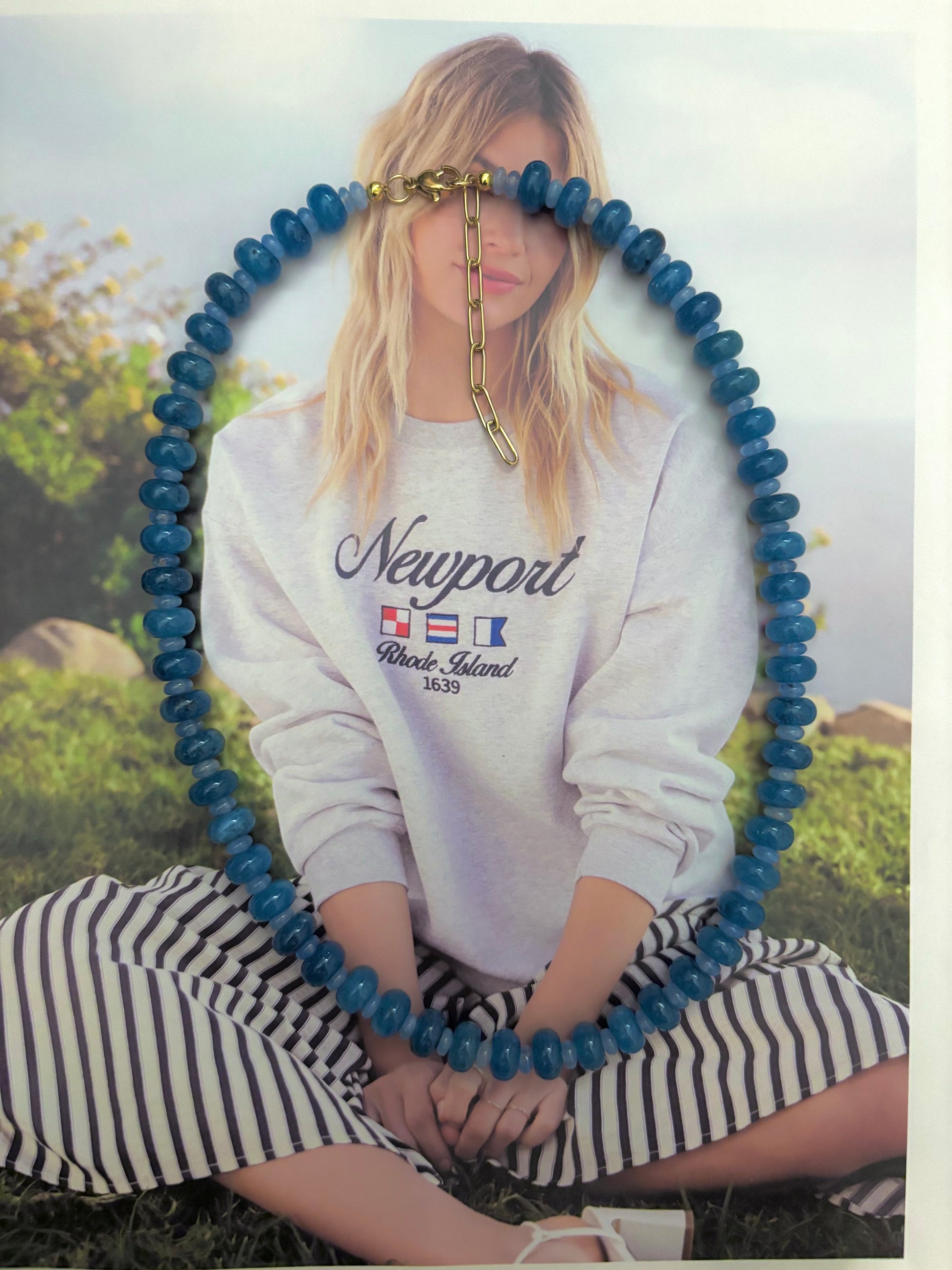 Chunky aquamarine beaded necklace displayed over a model in a Newport Rhode Island sweatshirt. The necklace features smooth aquamarine rondelle beads and an 18k gold plated chain with a 2-inch extender. Coastal-inspired jewelry perfect for layering or wearing solo. Handmade beach necklace with bold ocean blue stones, ideal for summer outfits, coastal weddings, or statement jewelry lovers. Soul Wave Beach Co. exclusive.