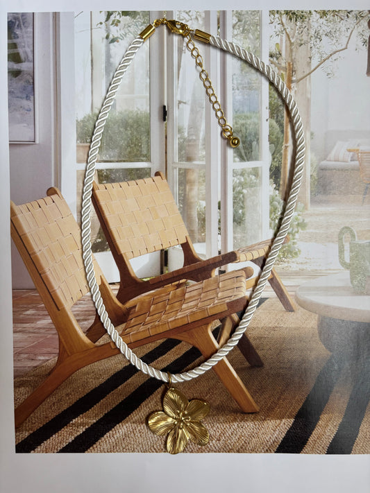 Chunky twisted white cord necklace with a large gold hibiscus-style flower pendant, styled on a neutral modern beach interior with woven chairs and natural light. Handmade by Soul Wave Beach Co, this tropical statement necklace features gold-plated hardware and an adjustable extender chain. A bold, retro-inspired piece for vacation outfits, beach weddings, or summer resort looks.

