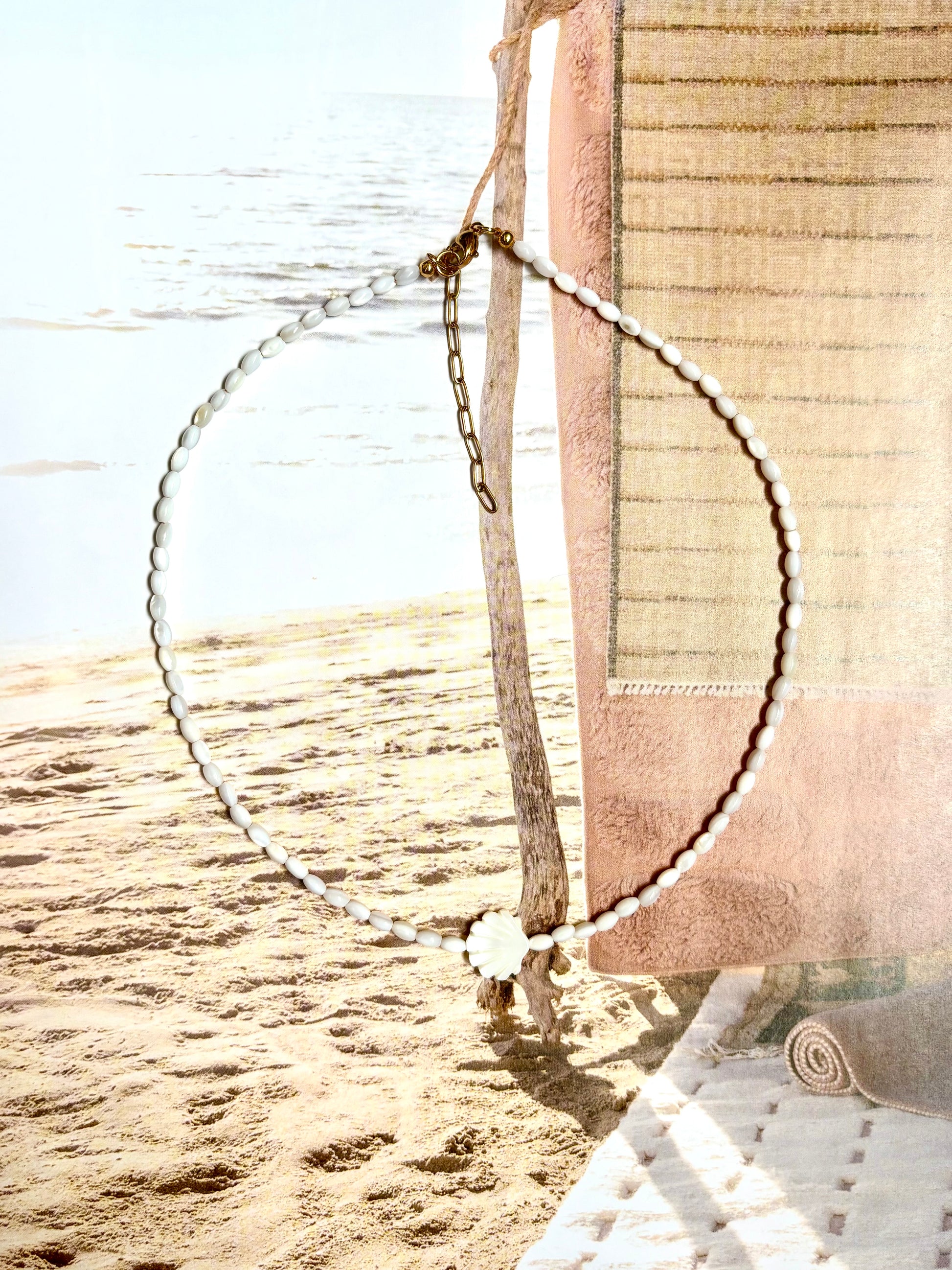 Coastal necklace made with natural mother of pearl beads and a carved shell centerpiece, photographed hanging by the beach with ocean waves and sand in the background. Features 14k gold-filled clasp and extender chain. Handmade by Soul Wave Beach Co, perfect for beachy, boho, or minimal summer styling.
