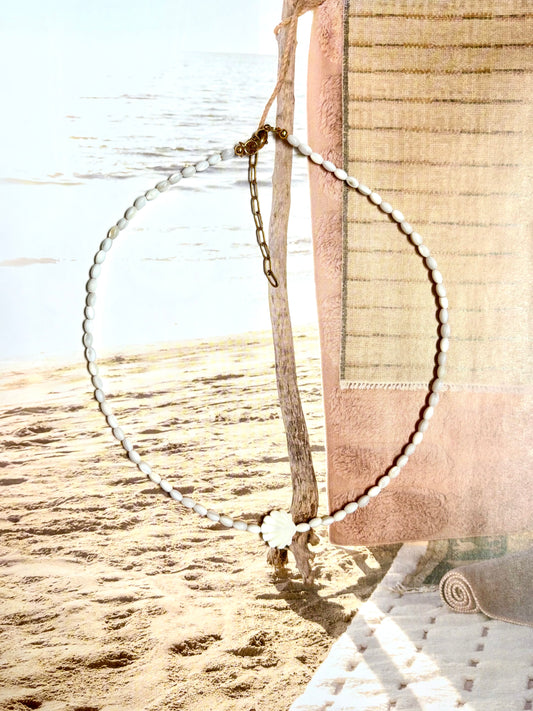 Coastal necklace made with natural mother of pearl beads and a carved shell centerpiece, photographed hanging by the beach with ocean waves and sand in the background. Features 14k gold-filled clasp and extender chain. Handmade by Soul Wave Beach Co, perfect for beachy, boho, or minimal summer styling.
